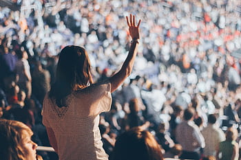 Diverse crowd enjoying a live event with one woman raising her hand in excitement. HD wallpaper