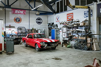 A vintage red car undergoing restoration in a well-equipped workshop with various tools and auto parts. HD wallpaper