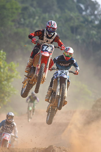 Exciting motocross race with bikers performing jumps on a dusty trail outdoors. HD phone wallpaper