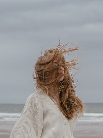 A serene moment of a young woman with wind-swept hair standing on a quiet beach, evoking peace and wanderlust. HD phone wallpaper