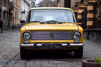 Front view of a vintage yellow car parked on a cobblestone street in Lviv, Ukraine. HD wallpaper