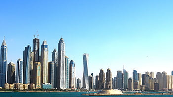 Panoramic view of Dubai's towering skyscrapers set against a vibrant blue sky and waterfront. HD wallpaper