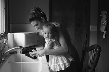 Black and white of a mother teaching her toddler to wash hands at a kitchen sink. HD wallpaper