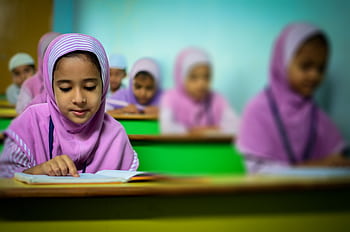 Group of young students in traditional hijabs focusing on their studies in a classroom. HD wallpaper