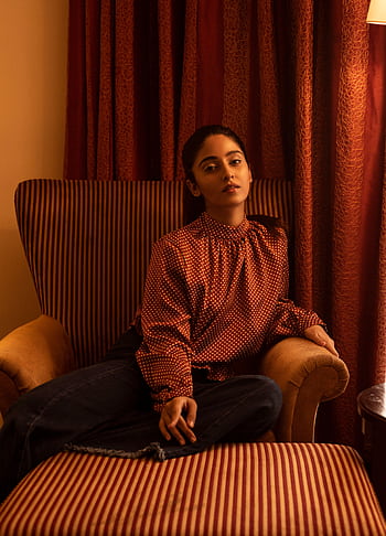 Sophisticated woman in a stylish outfit seated indoors in warm lighting. HD phone wallpaper