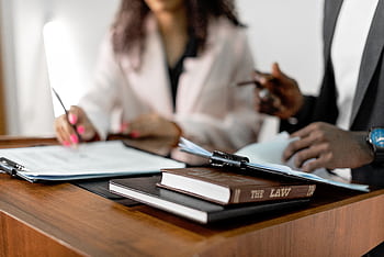 Two lawyers reviewing documents with law books on a desk. Professional legal environment. HD wallpaper