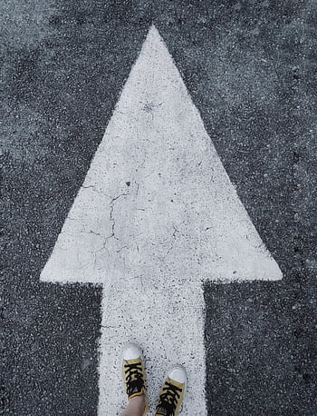 Top-down view of white arrow on asphalt with sneakers stepping forward. HD phone wallpaper