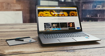 Laptop with open webpage on wooden desk, accompanied by tablet and pen, representing digital work setup. HD wallpaper