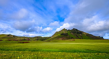 Stunning green landscape with rolling hills and a que mountain under a vibrant blue sky. HD wallpaper