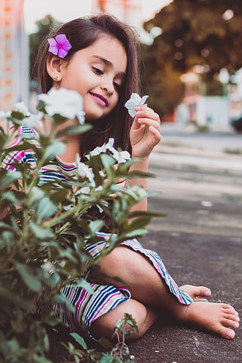 A cheerful young girl sitting outdoors, enjoying white flowers in Goiânia. HD phone wallpaper