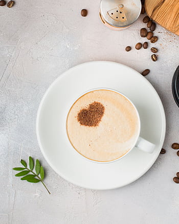 A cappuccino with a heart-shaped cocoa dusting on a saucer, surrounded by coffee beans. HD phone wallpaper