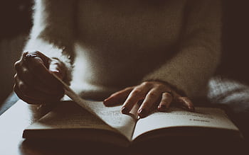 A person is reading a book in moody lighting, creating an intimate and reflective atmosphere. HD wallpaper