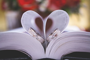 Close-up of wedding rings on heart-shaped book pages symbolizing love and romance. HD wallpaper