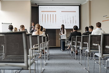 Business conference attendees listen to a presentation on revenue split by quarter and geography. HD wallpaper