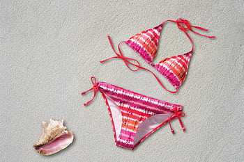 Colorful tie-dye bikini on sand next to a pink seashell, ideal for summer vibes. HD wallpaper