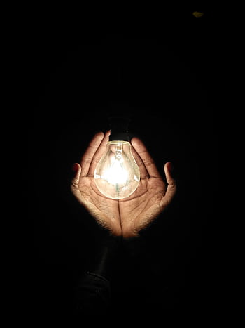A pair of hands gently cradles a glowing light bulb, illuminating the darkness. HD phone wallpaper