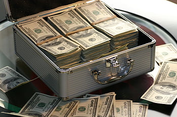 Open briefcase filled with stacks of hundred dollar bills on a glass table, representing wealth. HD wallpaper