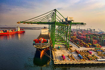 A bustling aerial view of a container port in North Jakarta, Indonesia with ships and cranes. HD wallpaper