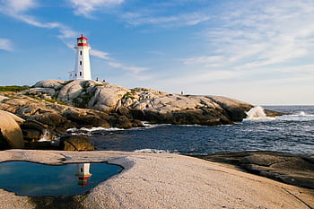 Lighthouse on rocky coast with ocean waves and bright sky, perfect for maritime themes. HD wallpaper