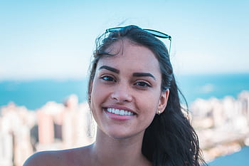 Portrait of a happy woman smiling with sunglasses on head, city skyline view. HD wallpaper