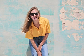 Casual young woman smiling in sunglasses, posing against a vintage colorful wall. HD wallpaper