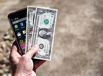 Close-up of a hand holding US dollar bills and a smart outdoors, showcasing financial technology. HD wallpaper