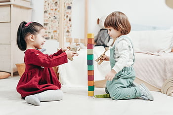 Two young children enjoying playtime with wooden blocks in a cozy indoor setting, fostering creativity and fun. HD wallpaper