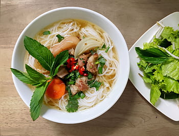 A fresh and vibrant bowl of Vietnamese Pho noodle soup with herbs and vegetables. HD wallpaper