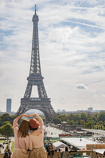 Tourists in Paris admire the iconic Eiffel Tower under a bright sky, capturing a moment of sightseeing and connection. HD phone wallpaper