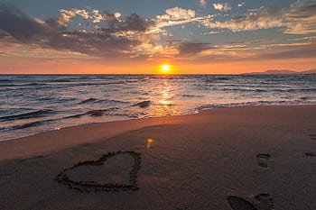 Beautiful sunset over ocean with a heart shape in the sand, perfect for romantic themes. HD wallpaper