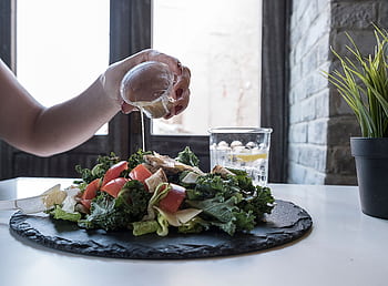 Hand pouring dressing over fresh salad with kale and tomatoes in a modern Dubai restaurant. HD wallpaper