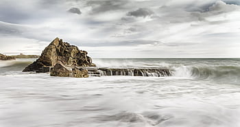 Capture of a rocky coastal cliff with stormy waves and a moody sky. HD wallpaper