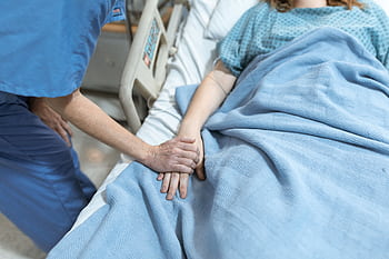 A nurse in scrubs offers comfort by holding a patient's hand in a hospital bed. HD wallpaper