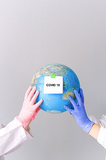 Hands in gloves hold a globe with 'COVID-19' label on a gray backdrop, symbolizing pandemic impact. HD phone wallpaper