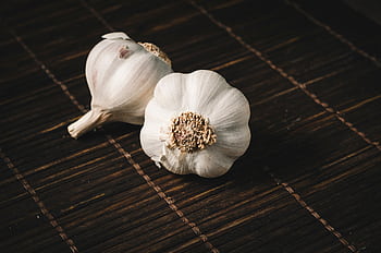 Two fresh garlic bulbs on a dark wooden mat, highlighting aromatic culinary ingredients. HD wallpaper