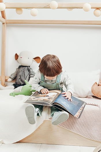 Adorable child reading a book in a cozy playroom, surrounded by toys. Perfect for early learning themes. HD phone wallpaper
