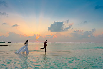 A couple enjoys a romantic moment running on a tropical beach during sunrise, capturing love and joy. HD wallpaper