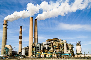 A large industrial power plant with smokestacks emitting smoke under a blue sky, symbolizing pollution. HD wallpaper