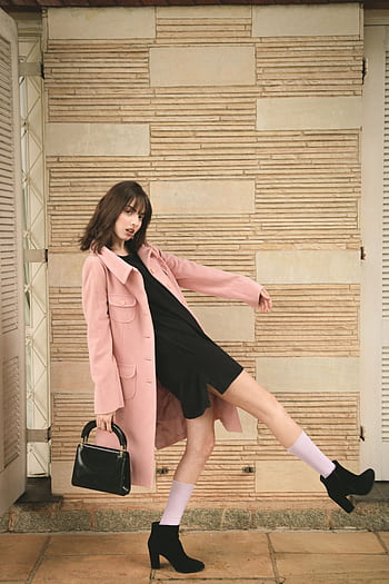 Fashion model in pink coat and black dress striking a dynamic pose indoors with stylish black heels. HD phone wallpaper