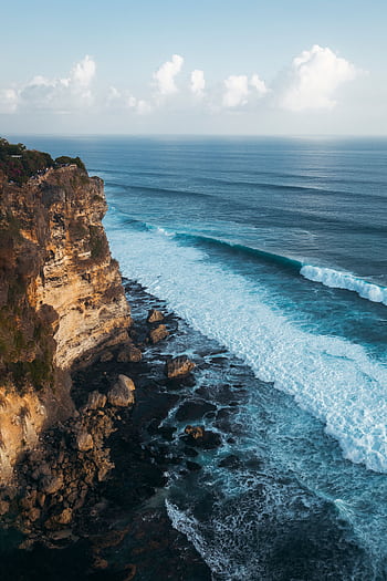 A breathtaking aerial view of Bali's rugged coastline showcasing waves crashing against towering cliffs under a clear sky. HD phone wallpaper