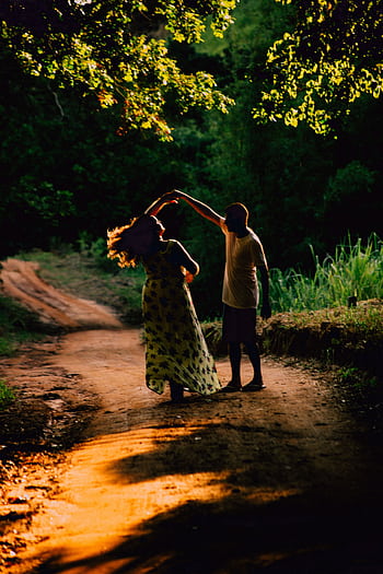 A couple gracefully dances on a sunlit dirt road surrounded by lush greenery in Saquarema, Brazil. HD phone wallpaper
