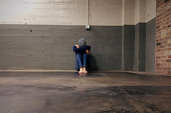 Person sitting in an empty room against a concrete wall, conveying solitude and despair. HD wallpaper
