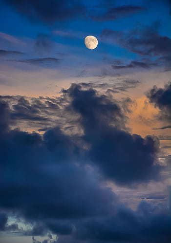 A captivating view of the moon amidst dramatic clouds at twilight, showcasing nature's artistry. HD phone wallpaper