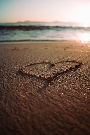 A heart shape drawn in the sand on a beach at sunrise with waves in the background. HD phone wallpaper