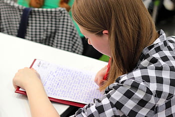 A young student writing in a notebook during a study session indoors. HD wallpaper