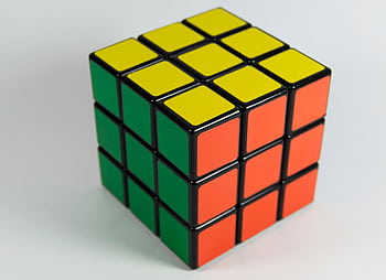 A solved Rubik's Cube displaying red, yellow, and green colors on a white backdrop. Perfect for puzzle enthusiasts. HD wallpaper