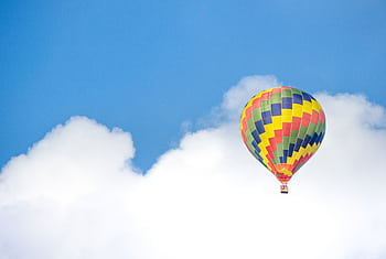 Colorful hot air balloon soaring amidst fluffy clouds on a sunny day. HD wallpaper