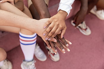 A group of friends stack their hands in unity on a sports court, symbolizing teamwork. HD wallpaper