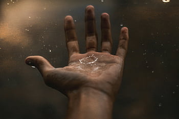 A close-up of an open hand catching raindrops against a dark background, showcasing water interaction. HD wallpaper