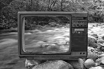 A vintage TV set frames a flowing stream in a tranquil forest setting, creating a nostalgic and artistic scene. HD wallpaper